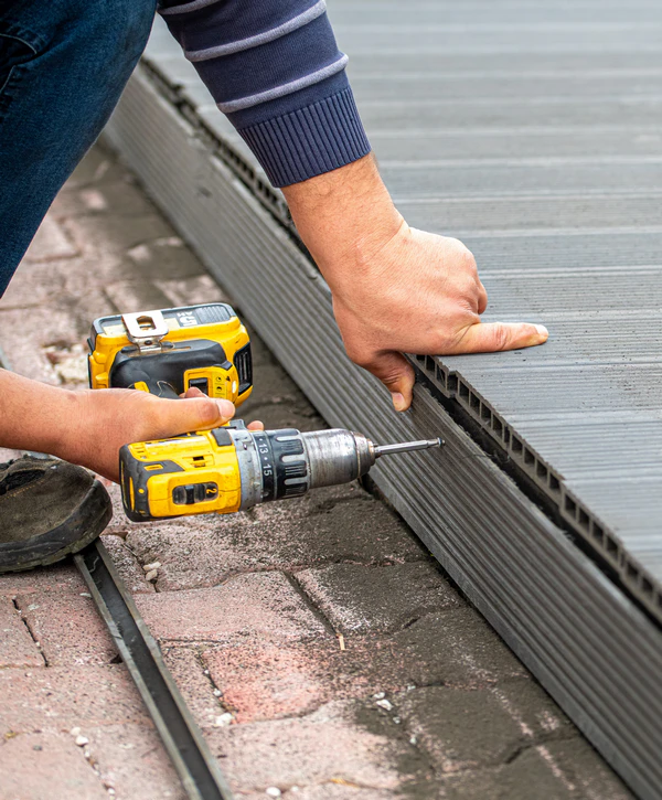 Close up of a contractor performing a composite deck repair in Chattanooga, TN by using a yellow power drill to secure grey decking boards with hidden fasteners.