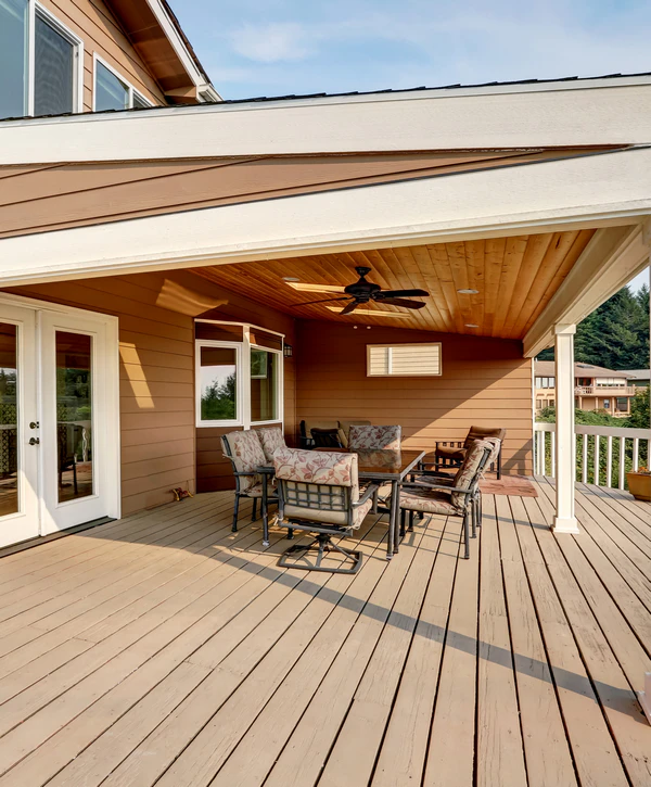 A covered deck installation in Chattanooga, TN, featuring a wood-paneled ceiling, a ceiling fan, white French doors, and an outdoor dining table set against brown house siding.