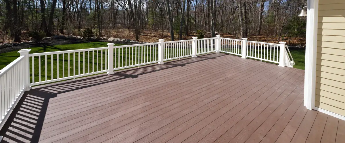 A beautiful custom-built natural wood deck featuring natural wood posts, railings with balusters, stairs, and a built-in gate. Nestled against a forest of evergreen trees in Chattanooga, TN. Shows a high-quality deck.
