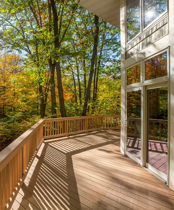 A bright custom wooden deck with railing casting shadows, overlooking a vibrant autumn forest, built by a deck builder in Chattanooga, TN.