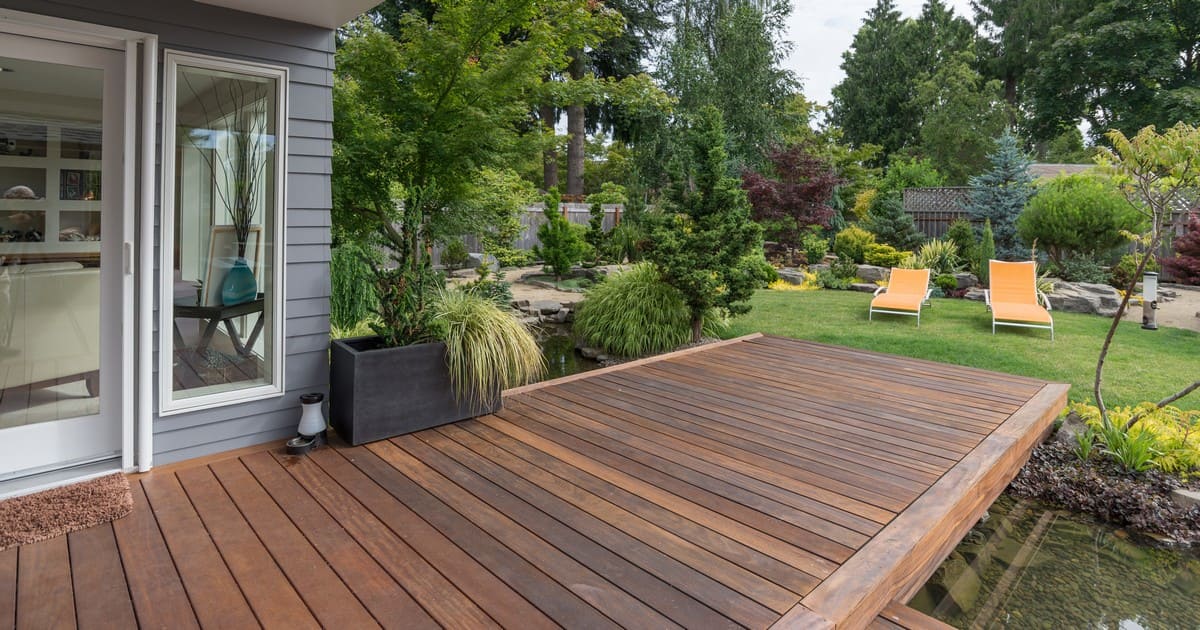 A beautifully landscaped backyard featuring a ground-level dark wood deck next to a water feature, showcasing an example of an outdoor living space to evaluate Deck Cost Chattanooga TN.
