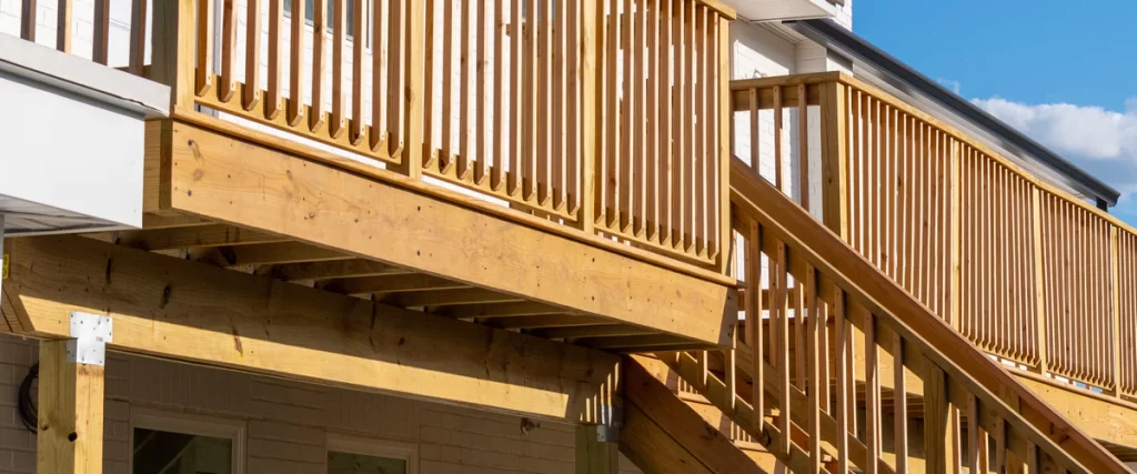 View from below of a raised wooden deck showing the sturdy structural framing, wooden stairs, and traditional vertical wood railings.