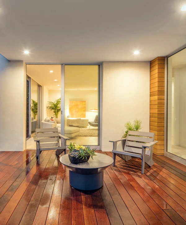 A beautifully polished wood covered patio with gray chairs and a succulent planter, showcasing a premium deck replacement in Chattanooga, TN outside a brightly lit living room.