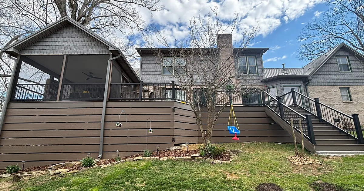 Custom elevated deck with screened porch, stairs, and black railing on backyard home addition