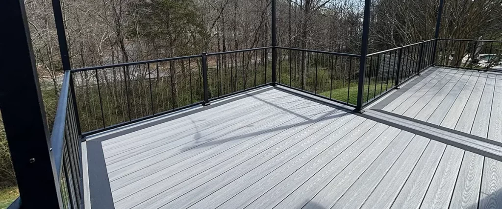 Gray composite deck with black aluminum railing overlooking wooded backyard and outdoor living area